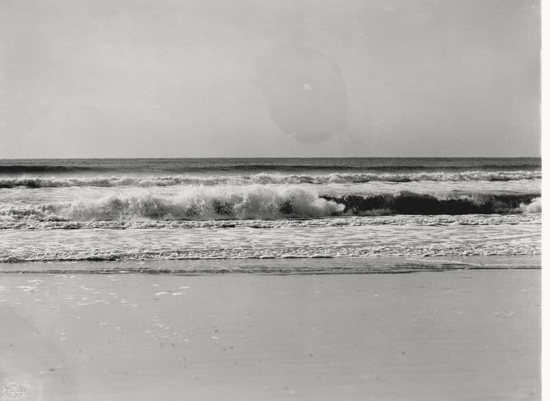 Ocean surf breaking in near-abstract bands of sky, foam, and wet sand.